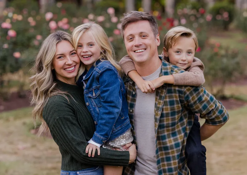 Chase and Christina smiling in a rose garden, Christina holding their daughter and their son riding on Chase's back