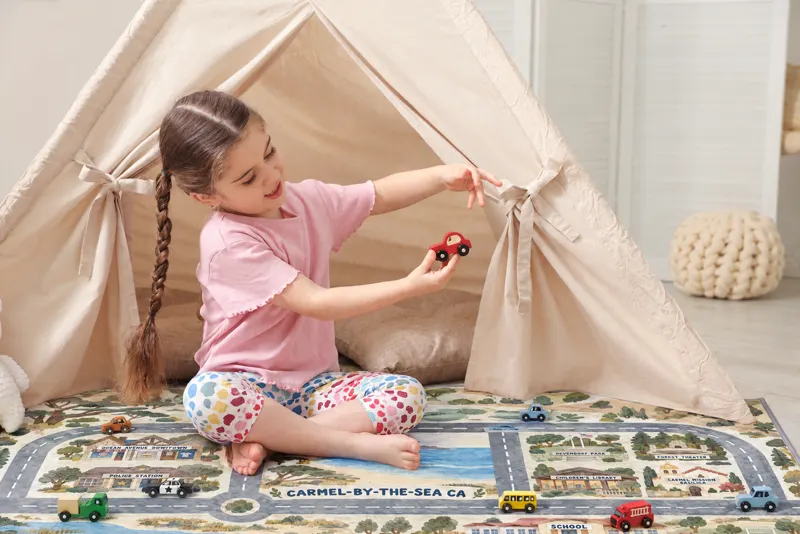 A girl by a play tent holding up a red toy car over her Carmel-by-the-Sea rug