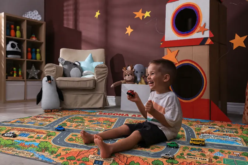 A laughing boy surrounded by toy cars on his red-rock Sedona rug