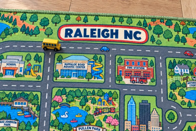 A close-up of the Raleigh rug's title banner and roads, with toy cars on them